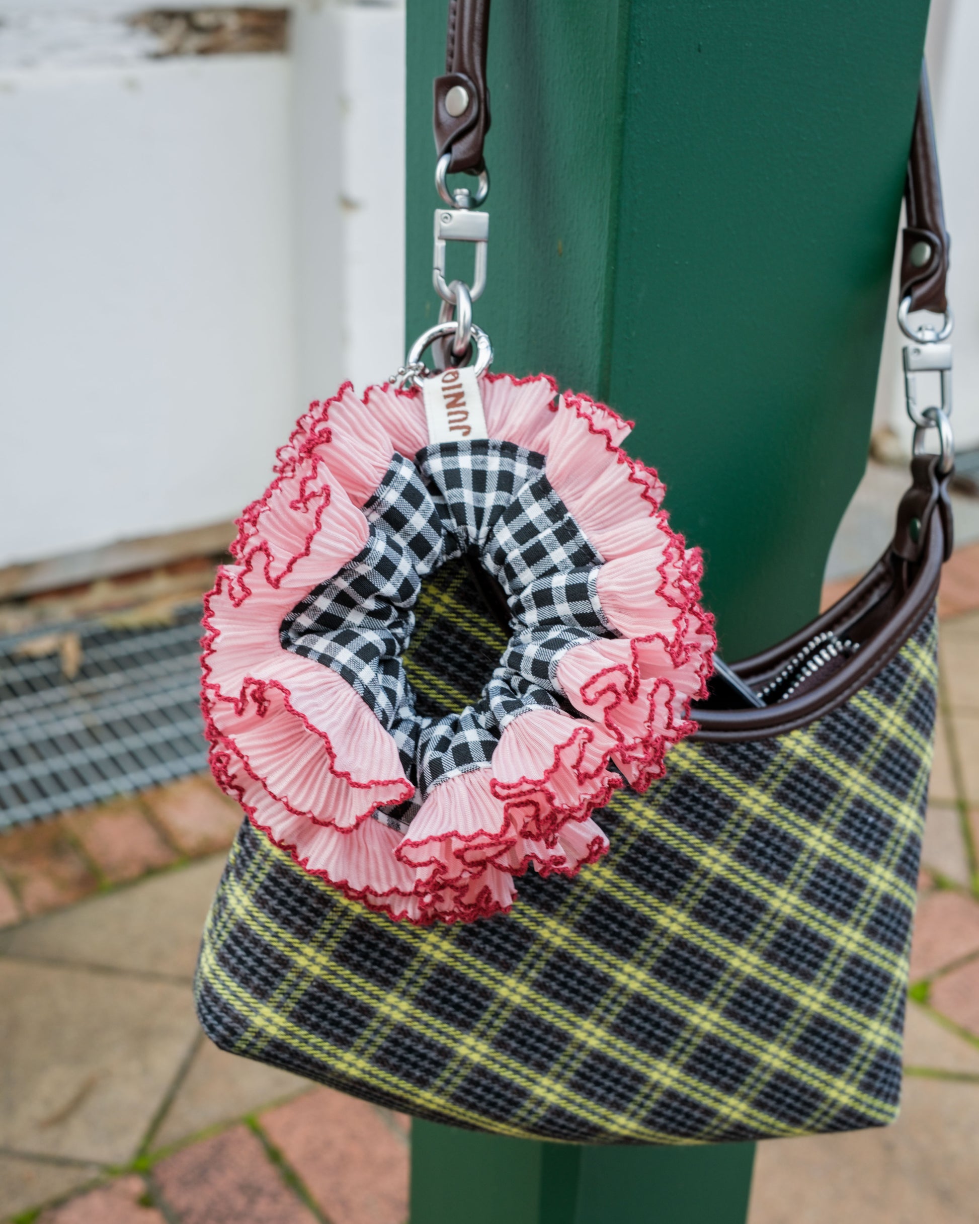 pink-black scrunchie keychain attached to a plaid bag with a blurred background