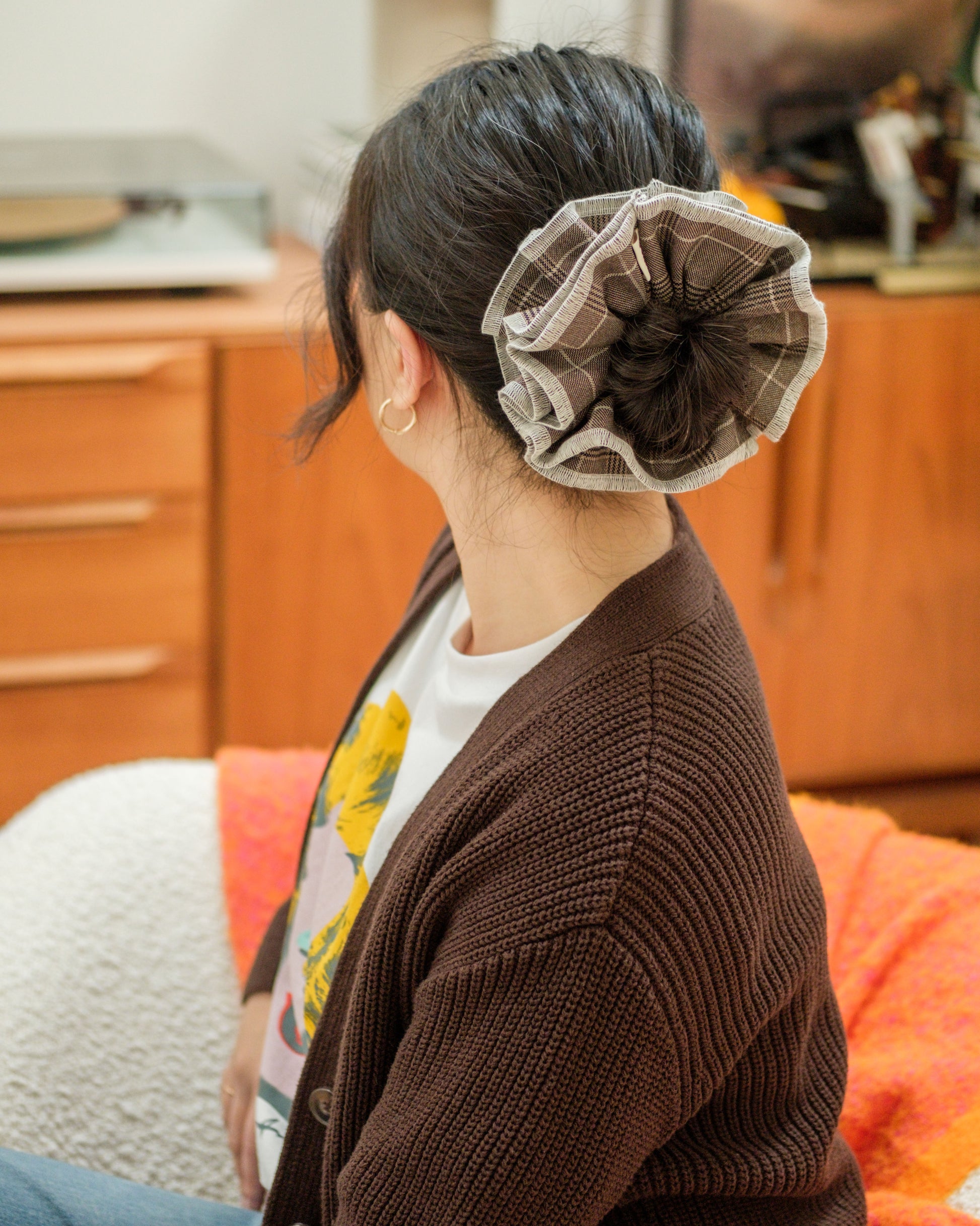 model wearing juniq brand scrunchie, brown color, glen plaid pattern, in her bun