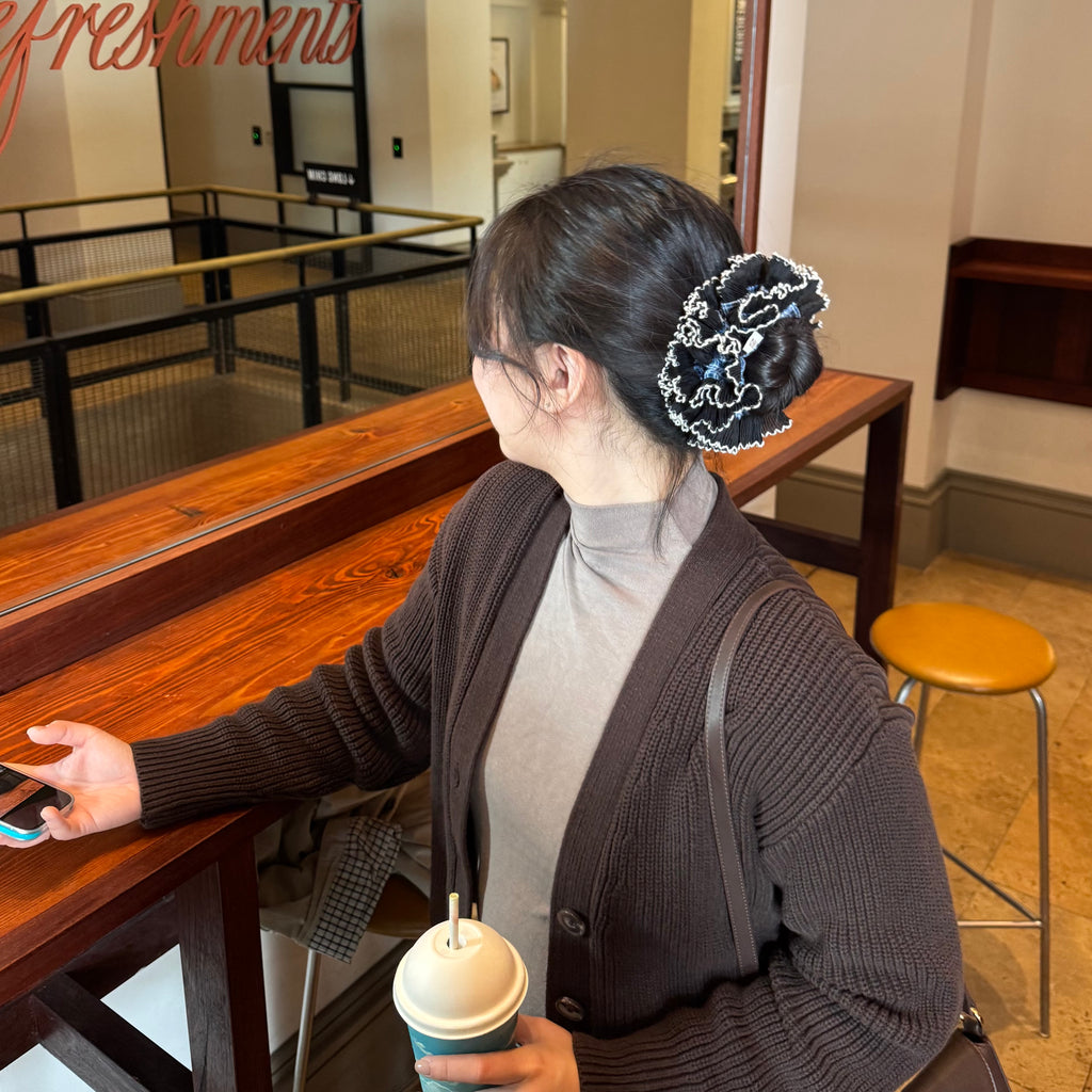 model wearing juniq brand scrunchie, double frilled, blue gingham, black ruffle trim, in her bun 