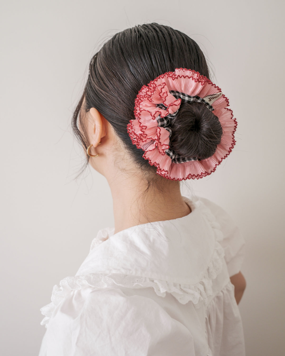 model wearing juniq brand scrunchie, double frilled, black gingham, pink ruffle trim, in her bun 