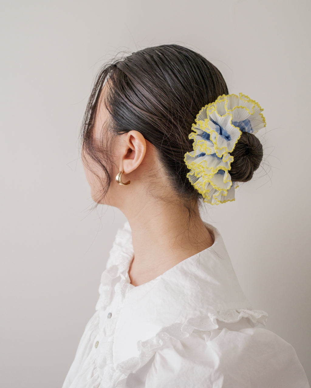 model wearing juniq brand scrunchie, double frilled, blue gingham, white/yellow ruffle trim, in her bun 