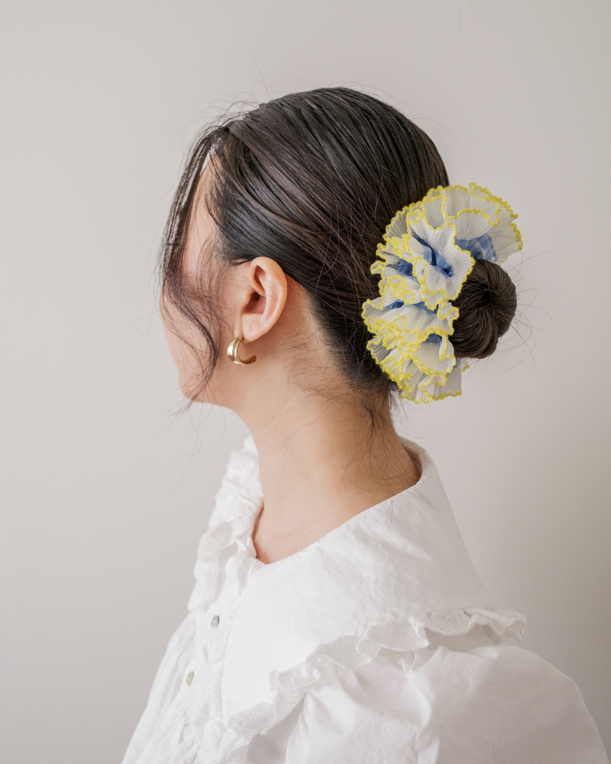 model wearing juniq brand scrunchie, double frilled, blue gingham, white/yellow ruffle trim, in her bun 