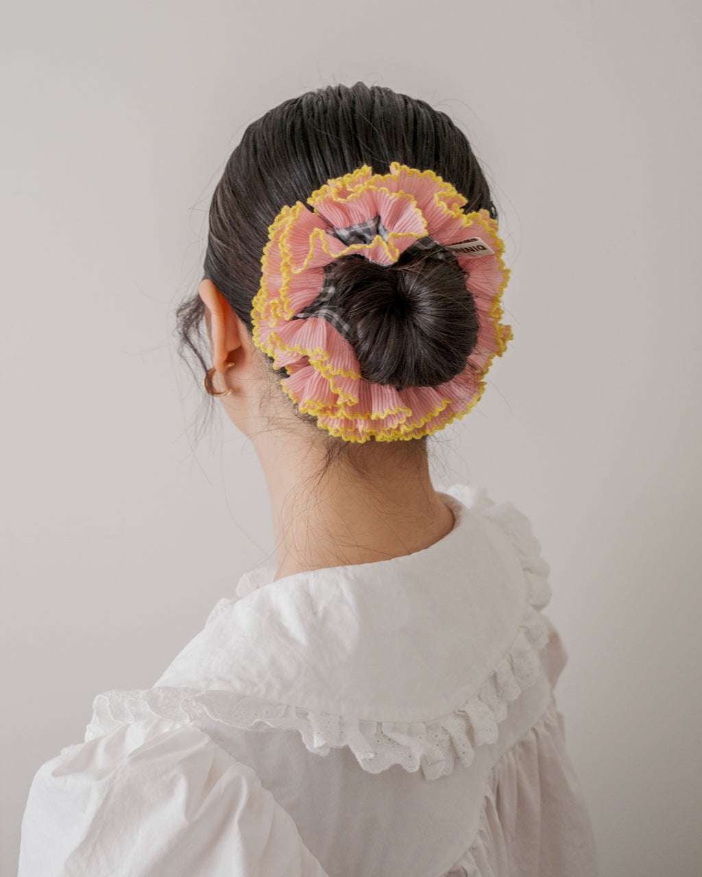 model wearing juniq brand scrunchie, double frilled, sage gingham, pink ruffle trim, in her bun 