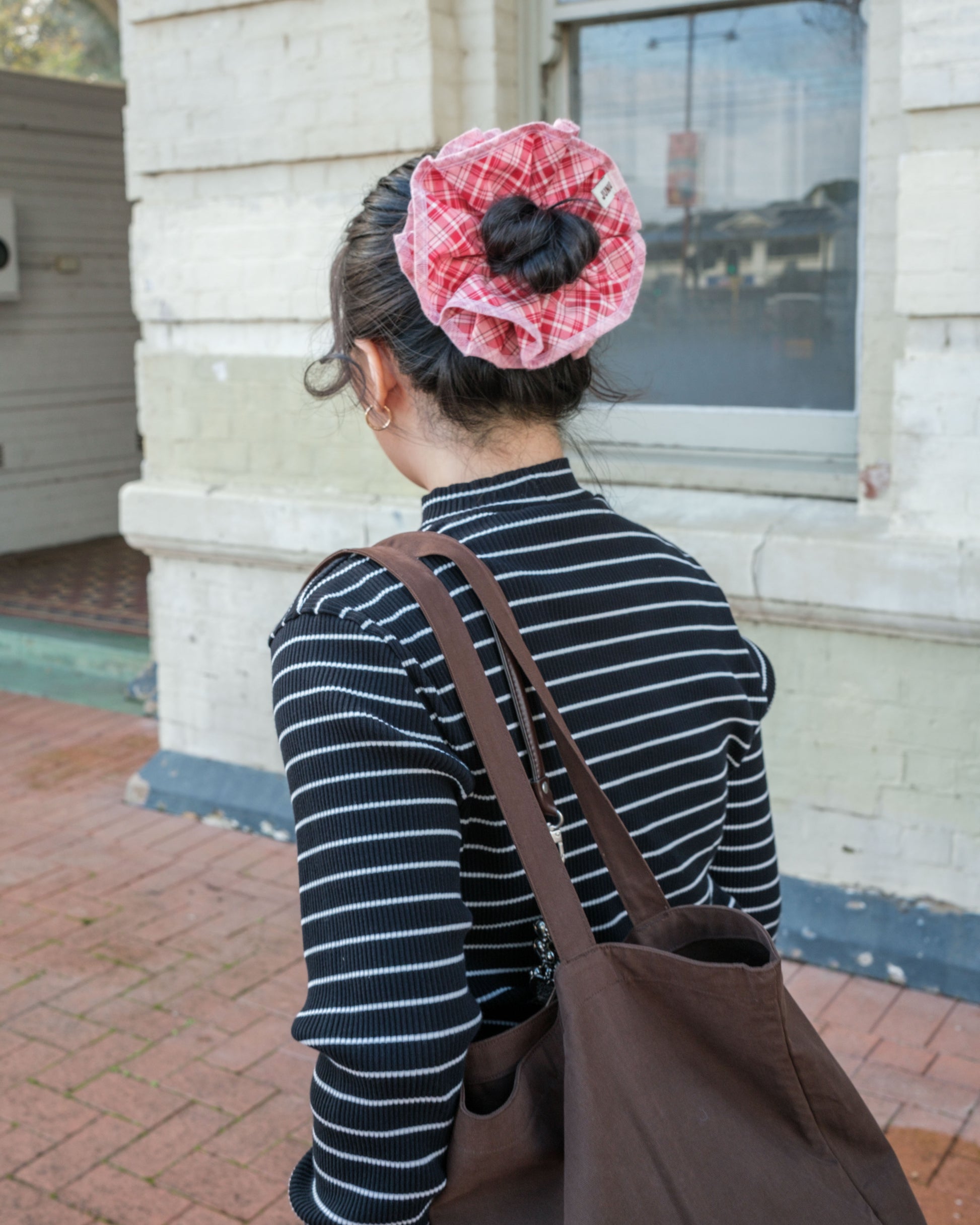 model wearing pink plaid juniq brand scrunchie on sidewalk